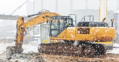 A Power Tan Wheel Loader Working At A Winter Construction Site In The Cold Weather With Light Snow Falling.